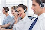 Attractive call centre agent with a headset with colleagues working around