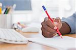 Man drawing with a red pencil on a desk besides a keyboard