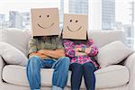 Funny workers with arms crossed wearing boxes on their heads with smiley faces on a couch