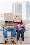 Funny workers with arms folded wearing boxes on their heads with smiley faces on a couch