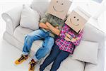 Silly employees with arms crossed wearing boxes on their heads with smiley faces on a couch