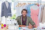 Attractive fashion designer drawing clothes and smiling to the camera