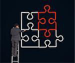 Businessman on a ladder drawing jigsaw puzzle on black background