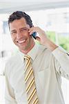 Businessman on the phone smiling at camera in office