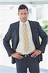 Serious businessman with hands on hips in office