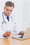 Doctor holding a bottle of pills and his using laptop