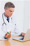 Attractive doctor holding a bottle of pills and using laptop