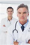 Serious doctor with arms crossed standing in front of his colleague