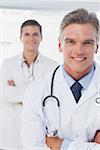 Smiling doctor with arms folded standing in front of his young colleague