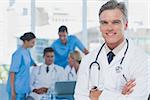 Handsome doctor with arms folded standing in front of a medical team