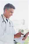 Grey haired doctor using digital tablet in a bright office