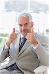 Happy businessman giving thumbs up in his office