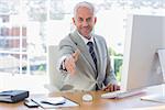 Smiling businessman reaching out arm for handshake at his desk