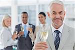 Businessman smiling at camera with champagne with team standing behind him