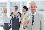 Businessman smiling at camera holding champagne with team behind him