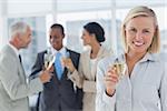 Businesswoman smiling at camera holding champagne with team behind her