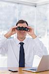 Businessman using binoculars in front of the camera in his office