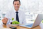 Happy businessman eating a salad on his desk during the lunch time