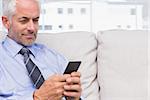 Cheerful businessman using smartphone on couch in staffroom