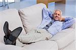 Businessman lying on sofa with his feet up smiling at camera in the office