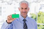 Happy businessman showing green business card in his office