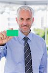 Smiling businessman showing green business card in his office