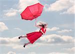 Attractive woman flying in the blue sky and holding a broken umbrella