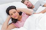 Woman covering ears while her husband is snoring next to her