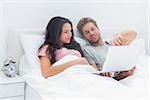 Couple lying in bed looking together at a laptop