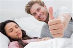 Man giving thumb up while his pretty wife is sleeping