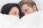 Couple under the duvet looking at each other in their bed