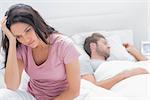 Anxious woman thinking in her bed next to her sleeping partner