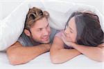 Couple under quilt smiling to each other