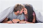 Cheerful couple head against head under the duvet in bed