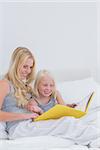 Cheerful mother and daughter reading a story together in bed