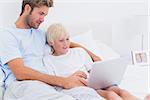 Father and son using a laptop in bed