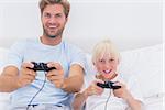 Father and son having fun playing video games in bed