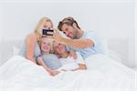 Cheerful family taking self pictures with a smartphone in bed