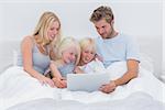 Beautiful family using a laptop lying in bed