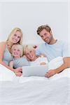 Cheerful family using a laptop lying in bed