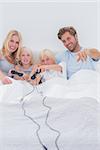 Cheerful family playing video games in bed