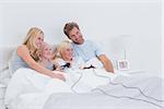 Siblings playing video games with parents watching in bed