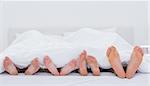 Family showing their feet while lying on bed