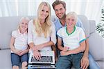 Cheerful family using laptop in the living room and looking at camera