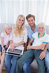 Smiling family using laptop in their living room and looking at camera