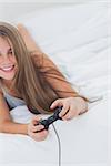 Cheerful young girl playing video games while she is lying on her bed
