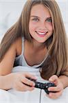 Portrait of a young girl playing video games while she is lying on her bed