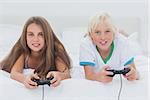 Portrait of siblings playing video games while they are lying on bed