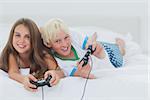 Cheerful siblings playing video games while they are lying on bed