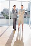 Confident businesswomen standing in bright office with arms crossed